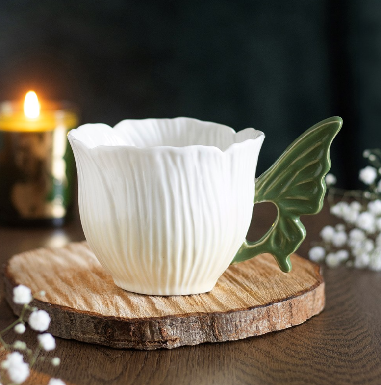 Flower-shaped ceramic teacup with green fairy wing handle.